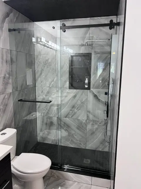 Stylish walk-in shower renovation featuring dark tile flooring, frameless glass enclosure, rainfall showerhead, and modern bathroom fittings