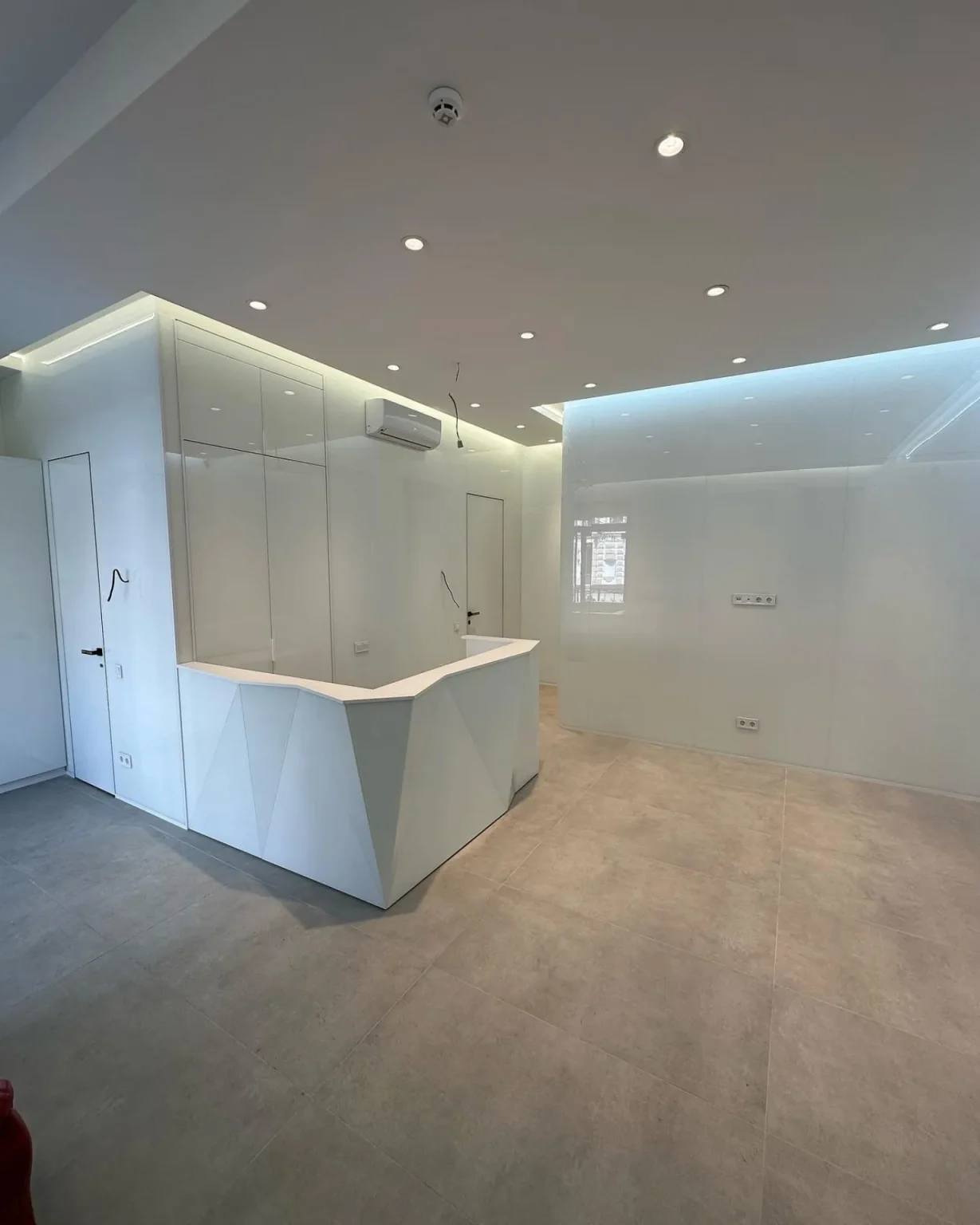 Commercial interior space with geometric white reception desk, LED cove lighting, and glossy wall panels in a clean modern design