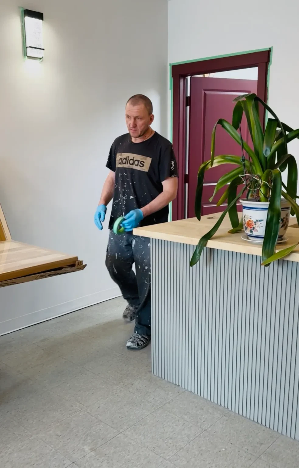 Worker in progress on modern reception renovation featuring vertical slat counter design, natural wood top, and red door accents