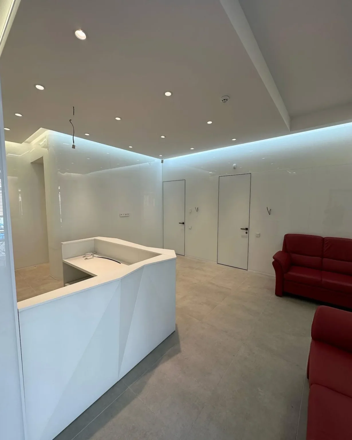 Renovated commercial waiting area with modern reception desk, LED ceiling lighting, and white gloss panel walls paired with red seating