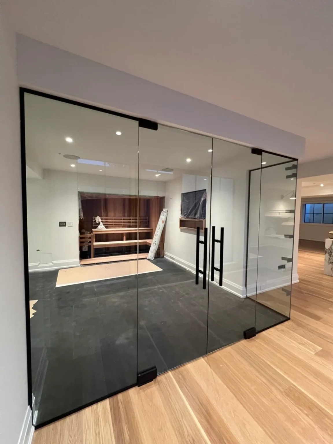 Residential home gym renovation featuring full-height glass wall with double glass doors, recessed lighting, and wood flooring by Loon Renovation in Ontario