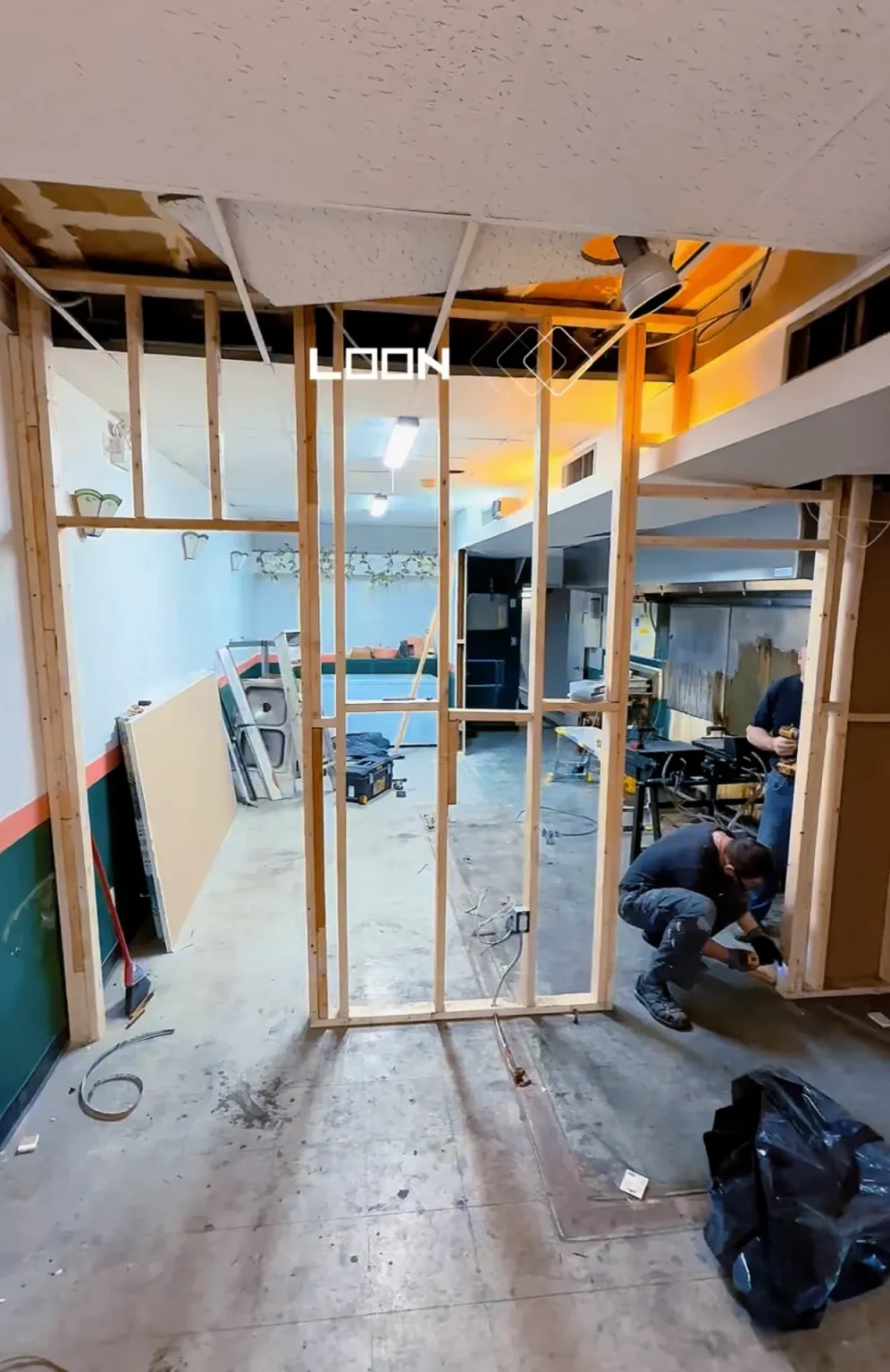 Commercial interior renovation in progress with open wall framing, tools on-site, and ceiling demo underway during framing stage