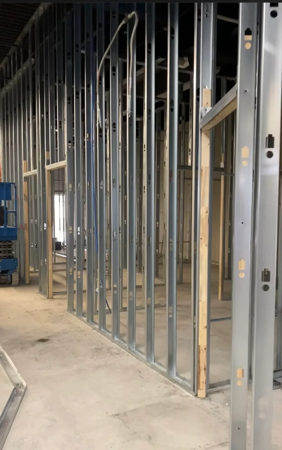 Close-up of steel stud framing for partition walls in a commercial interior renovation with visible utility conduit and lift in background