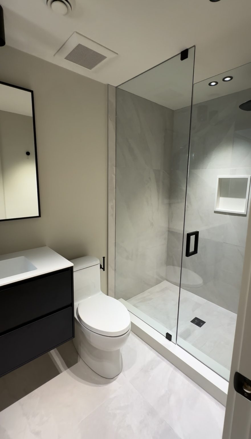 Modern bathroom renovation featuring a black floating vanity, frameless glass shower with matte black hardware, and large marble-style wall tiles