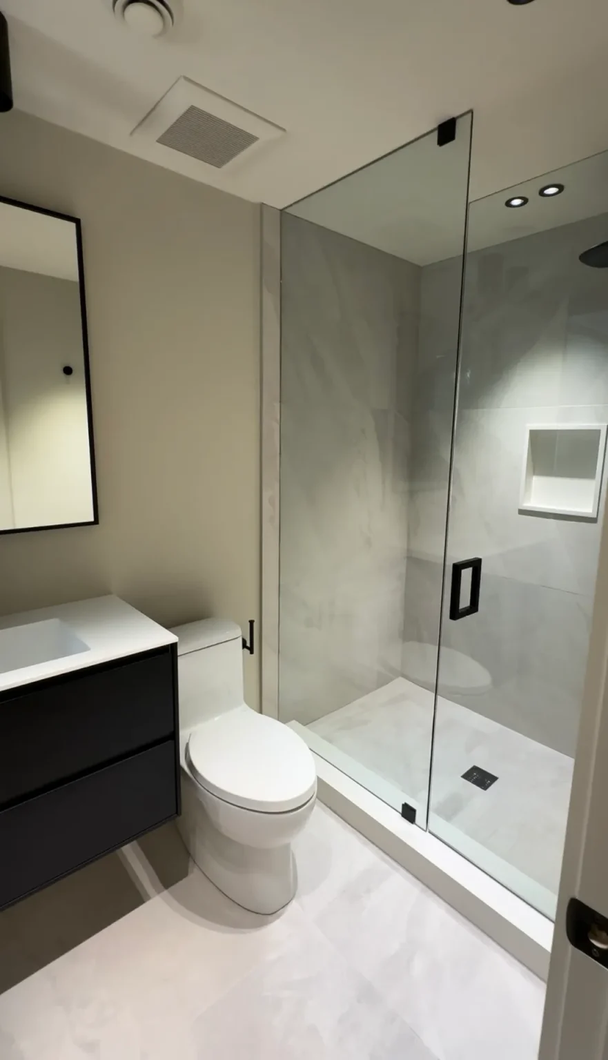 Elegant bathroom renovation featuring a black wall-mounted vanity, frameless glass shower, and light tile flooring by Loon Renovation in Ontario