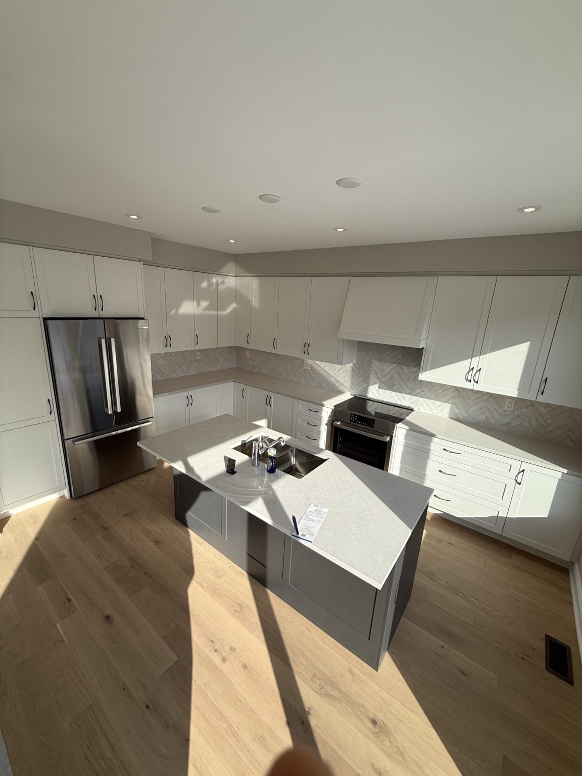 Modern cottage kitchen renovation showcasing white shaker cabinets, quartz countertops, and a gray center island with a stainless steel sink and appliances