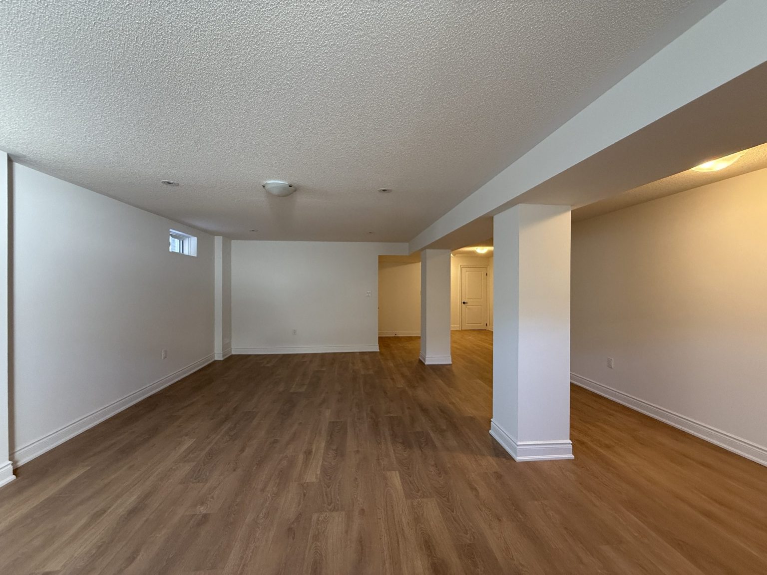 Renovated basement featuring wood-look vinyl flooring, recessed lighting, white columns, and a clean open-concept layout ideal for multipurpose use