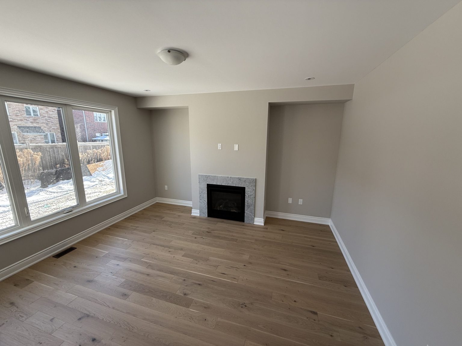 Bright living room with newly installed oak flooring, large windows for natural light, and a clean-lined fireplace with stone surround