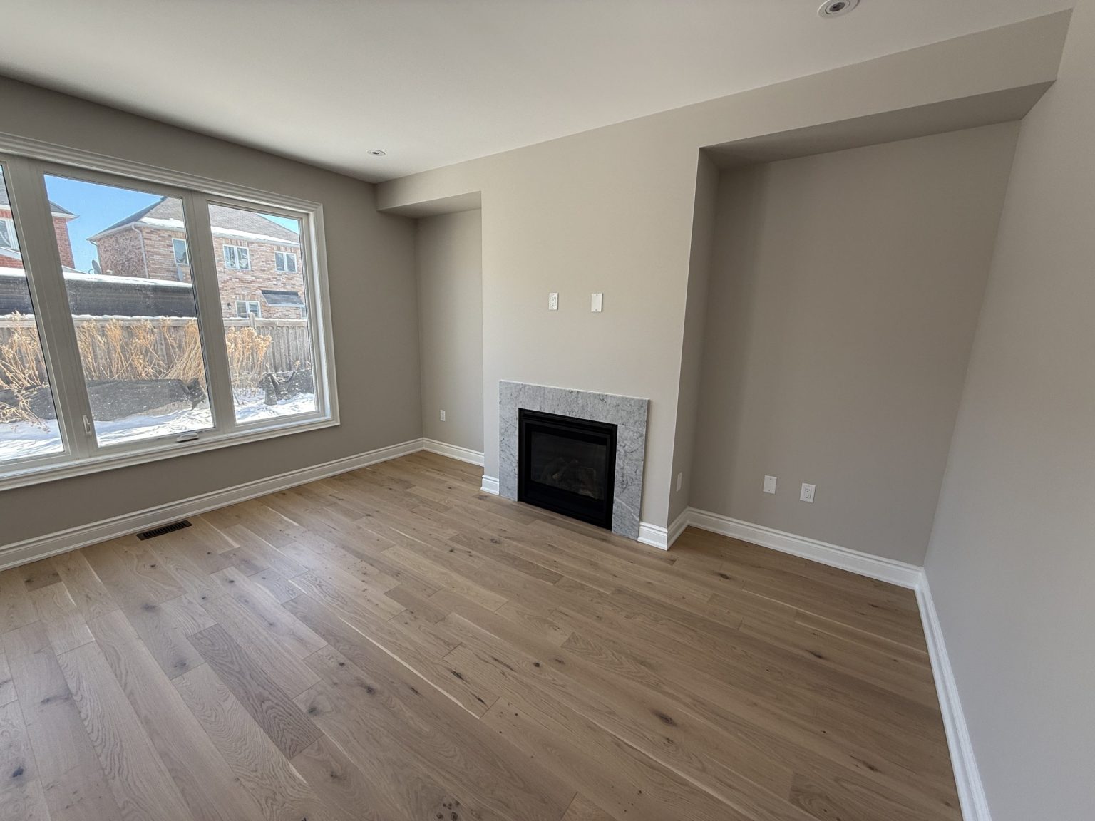 Renovated living room featuring new hardwood floors, neutral wall tones, a built-in gas fireplace with stone surround, and a large front-facing window