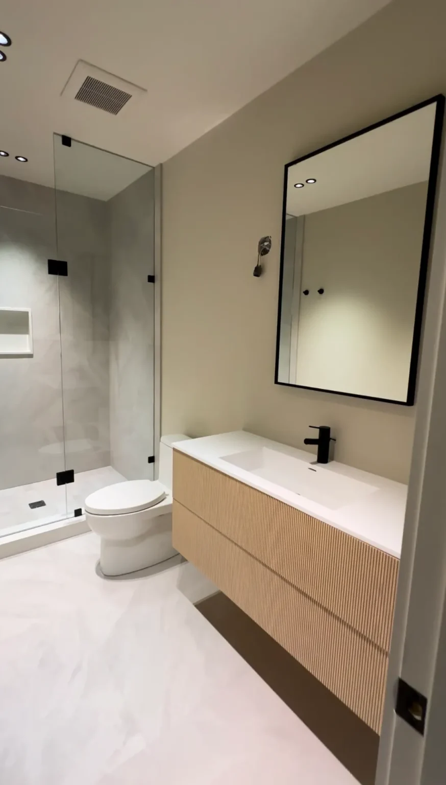 Minimalist bathroom renovation featuring floating fluted vanity, walk-in shower with glass enclosure, and matte black fixtures in Ontario