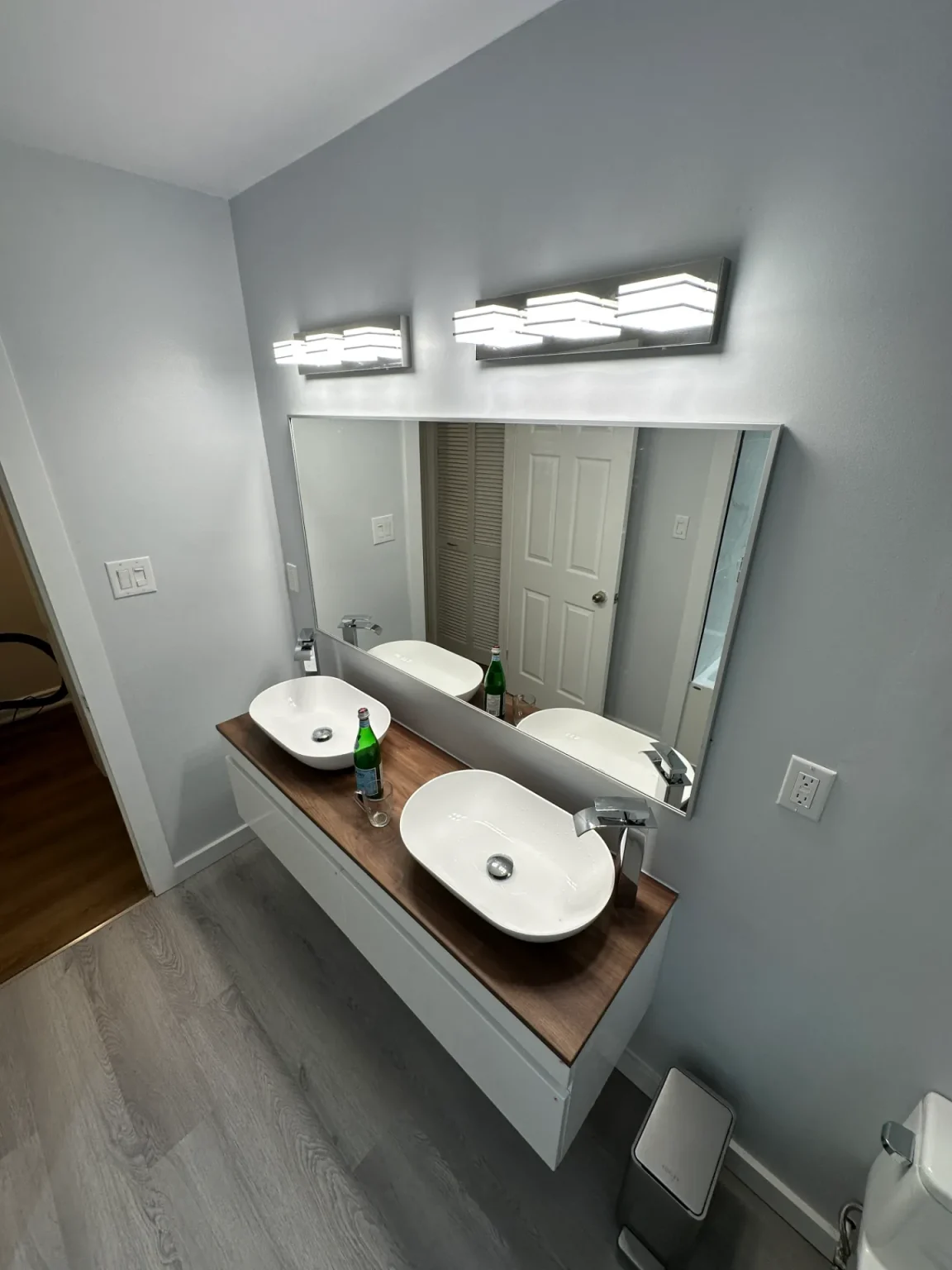 Contemporary bathroom renovation with wall-mounted vanity, double vessel sinks, and backlit mirror by Loon Renovation in Ontario