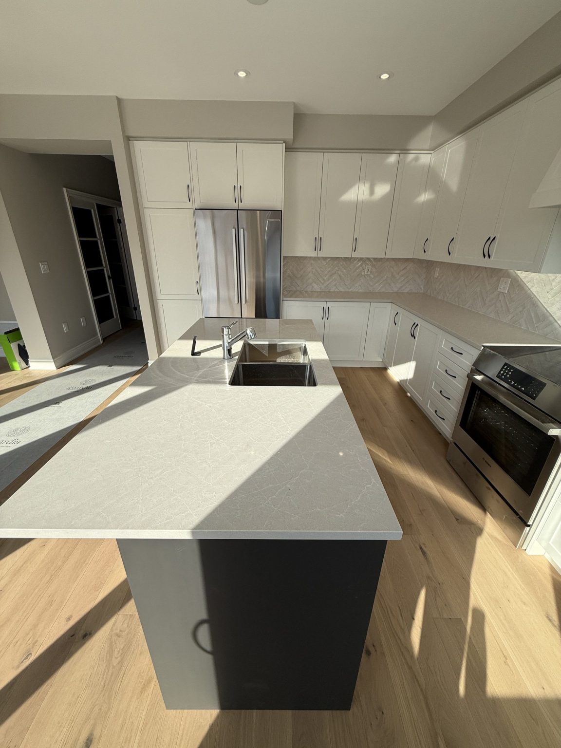 Cottage kitchen renovation showcasing a spacious quartz island with undermount sink, black base cabinetry, and light wood flooring for a modern look