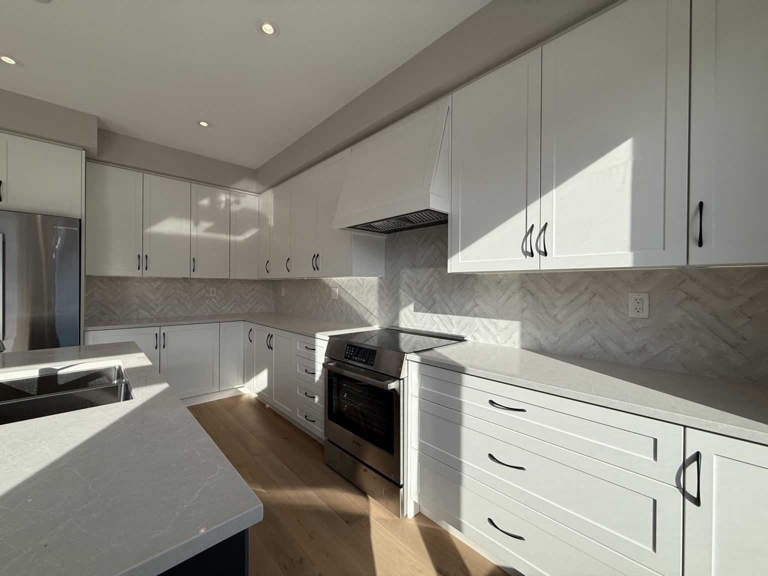 Stylish cottage kitchen renovation featuring white quartz countertops, stainless steel appliances, and herringbone tile backsplash under natural light