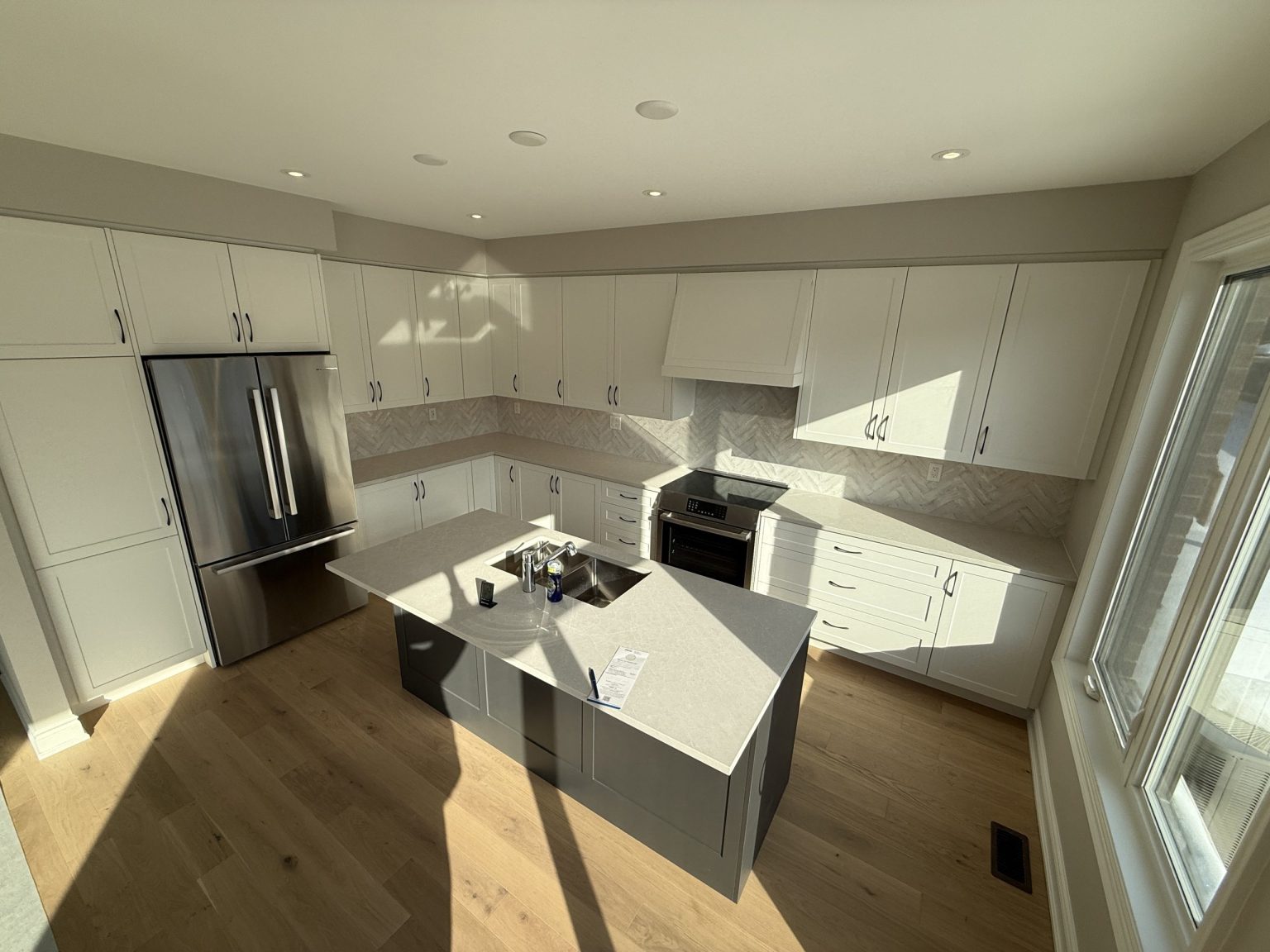 Renovated cottage kitchen featuring full-height white cabinetry, quartz countertops, a gray island, and natural wood flooring with ample sunlight