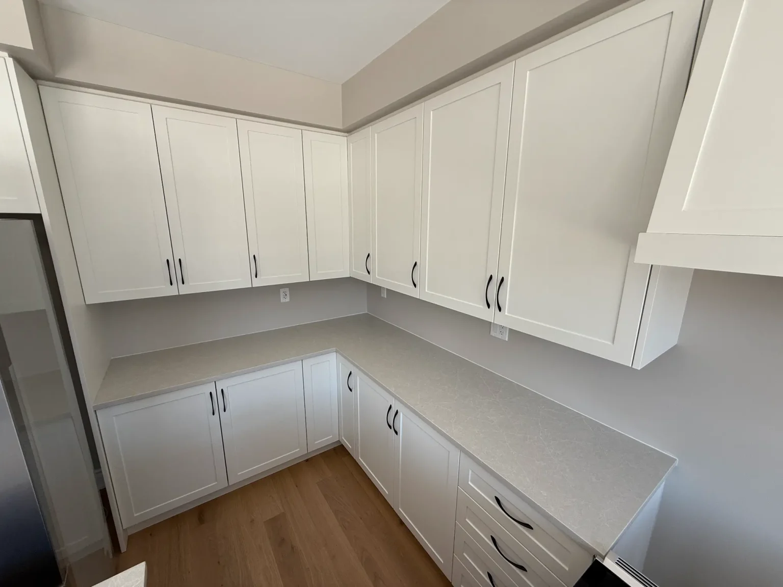 Contemporary kitchen design showcasing white shaker-style cabinets, smooth light-toned quartz countertops, and matte black hardware in a clean layout