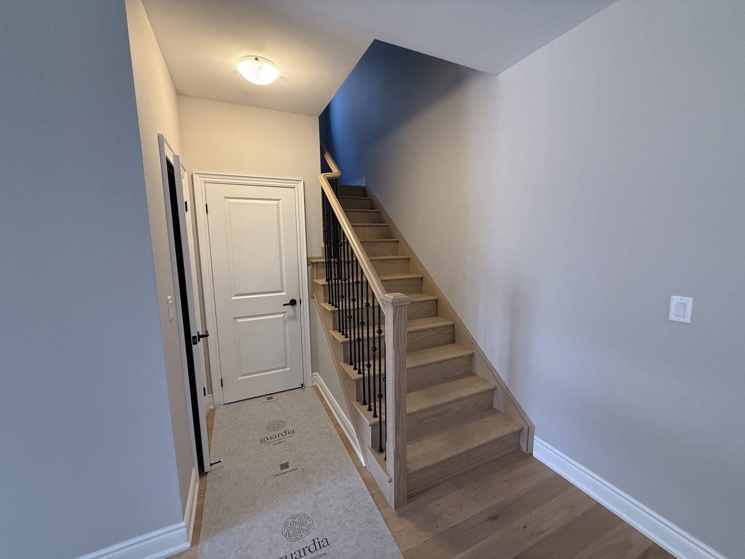 Newly remodeled home entryway featuring natural oak stairs, black iron spindles, and clean white doors against soft neutral walls
