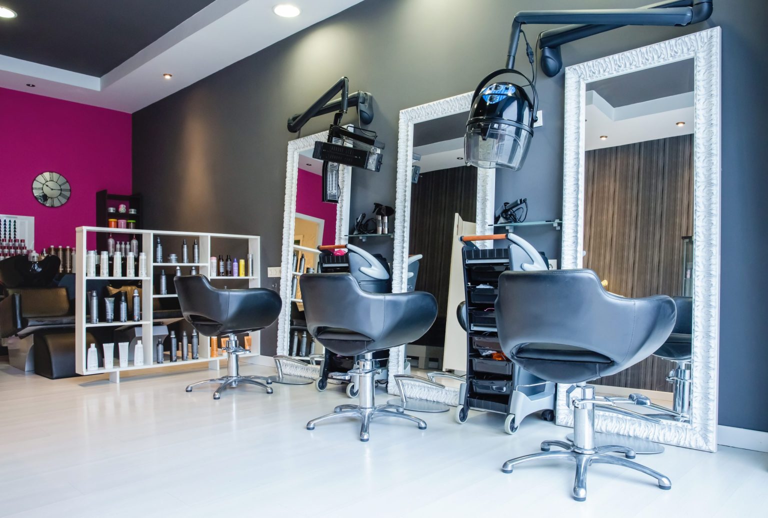 Renovated salon featuring sleek black chairs, large mirrors, mounted hair dryers, and vibrant pink and grey walls