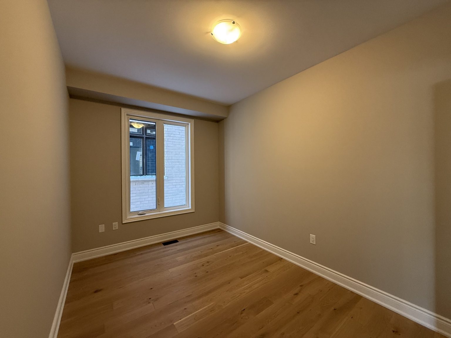 Compact bedroom remodel featuring warm hardwood flooring, soft beige walls, recessed window framing, and a ceiling-mounted light fixture