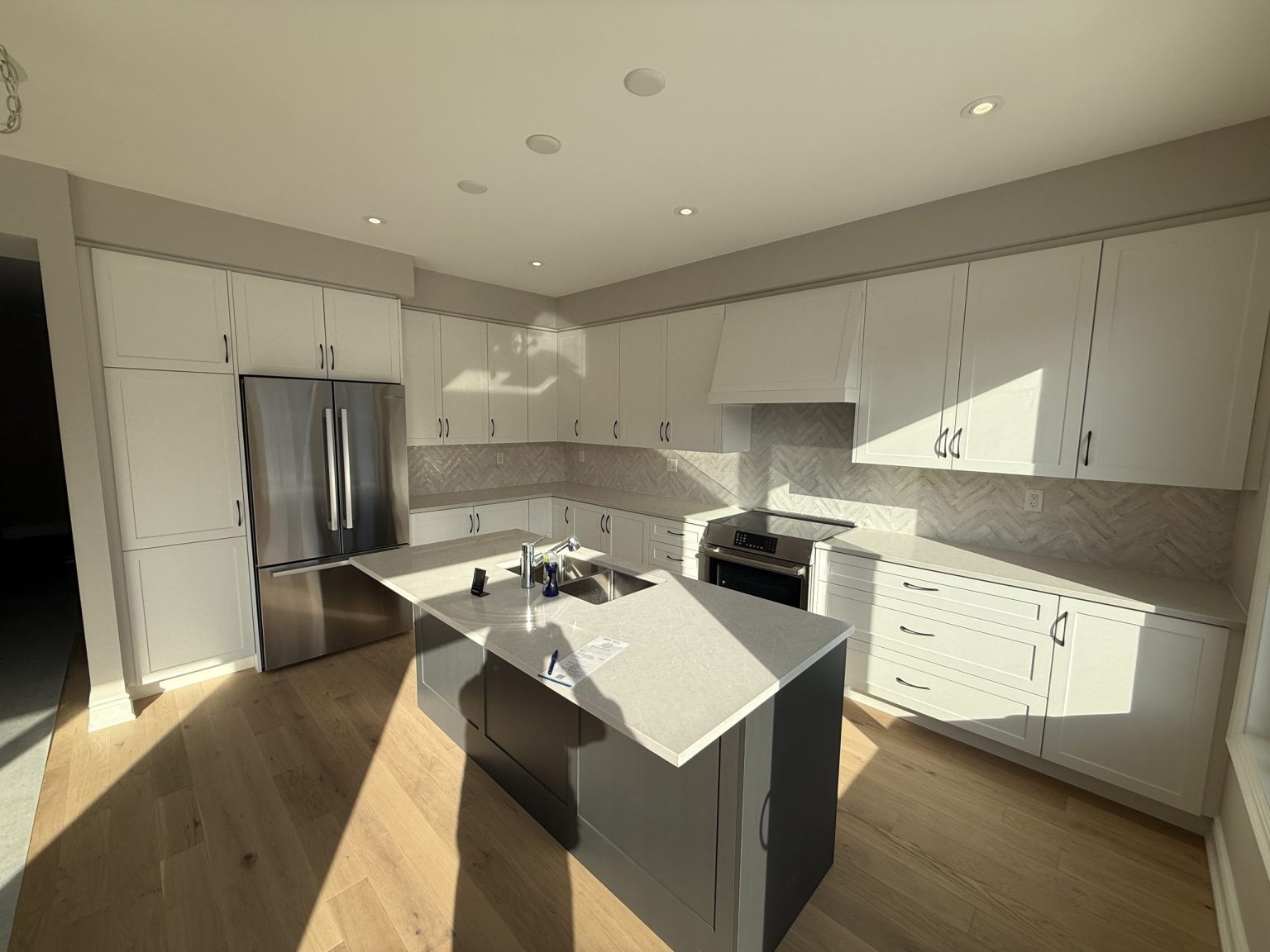 Elegant cottage kitchen renovation showcasing white shaker cabinets, grey center island, and herringbone backsplash under natural sunlight