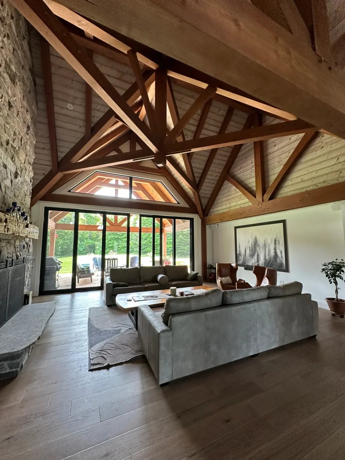 Renovated cottage living room showcasing vaulted wood ceiling, timber trusses, stone fireplace, and large sliding doors opening to a patio