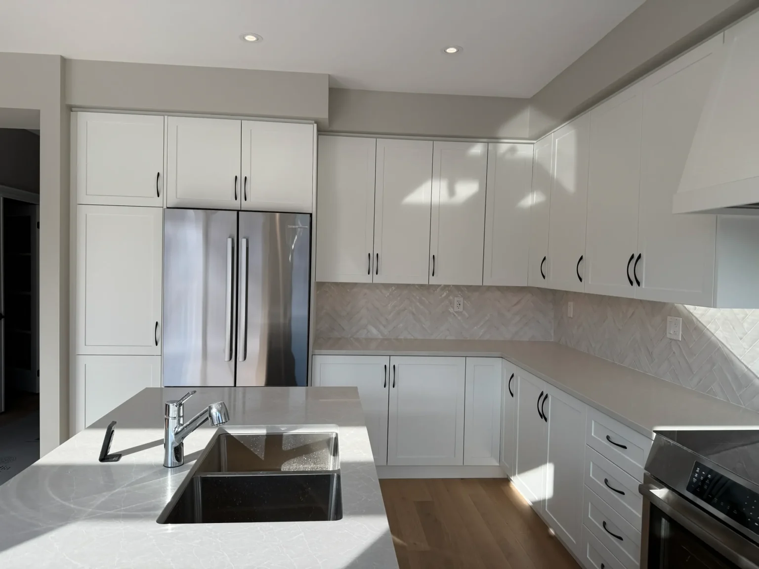 Bright cottage kitchen renovation featuring white quartz counters, undermount stainless steel sink, and shaker-style cabinets with matte black handles